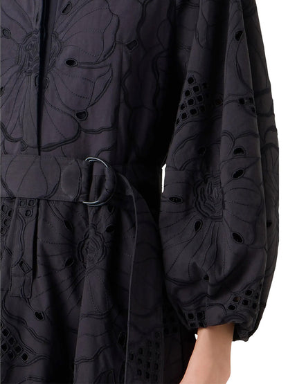Close-up of a person wearing the Akris Punto Flower Eyelet Embroidered Midi Dress in Black, featuring floral embroidery, eyelet details, and a belted waist; only the torso and part of one arm are visible.