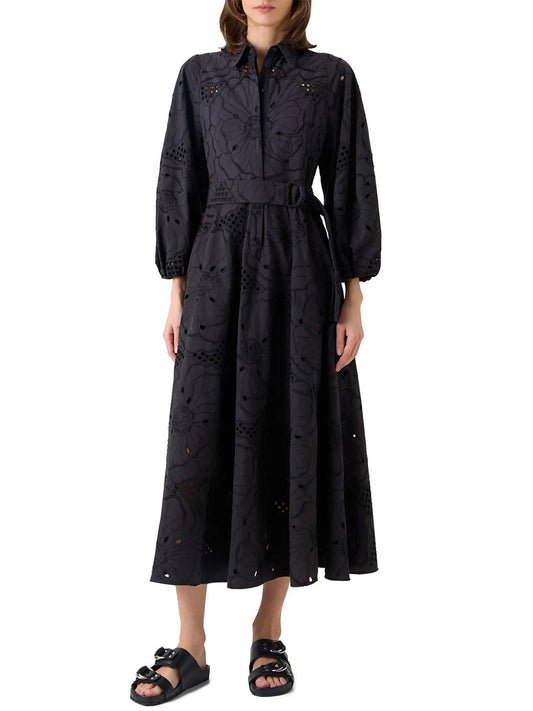 A woman wears the Akris Punto Flower Eyelet Embroidered Midi Dress in black with long sleeves, a collar, and a belt, paired with black sandals, standing against a plain background.