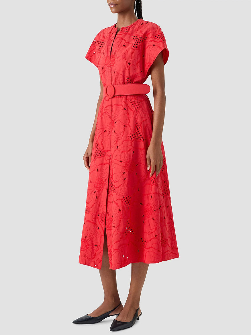 A woman wearing the Akris Punto Flower Eyelet Embroidered Midi Dress in red and black pointed flats stands against a light gray background.