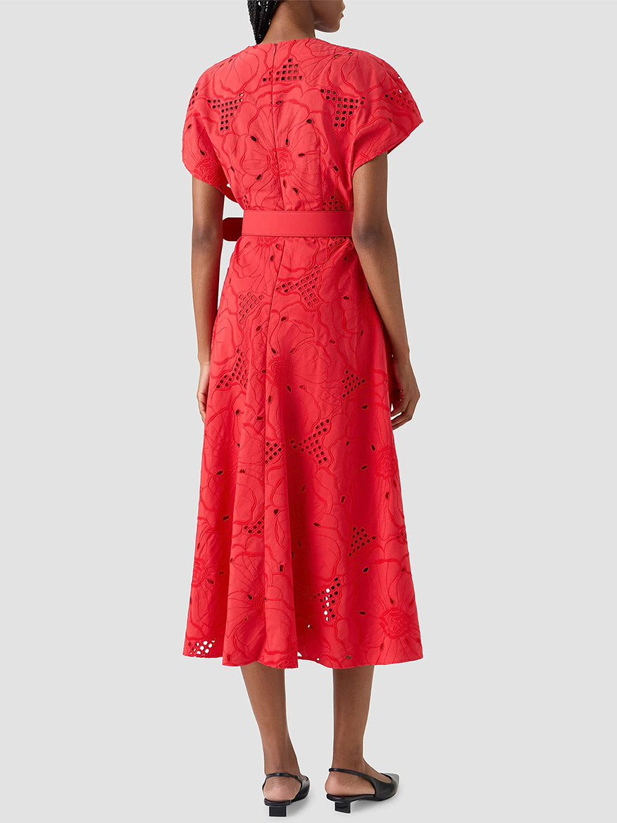 A woman faces away, wearing the Akris Punto Flower Eyelet Embroidered Midi Dress in red with a matching belt, paired with black flats.