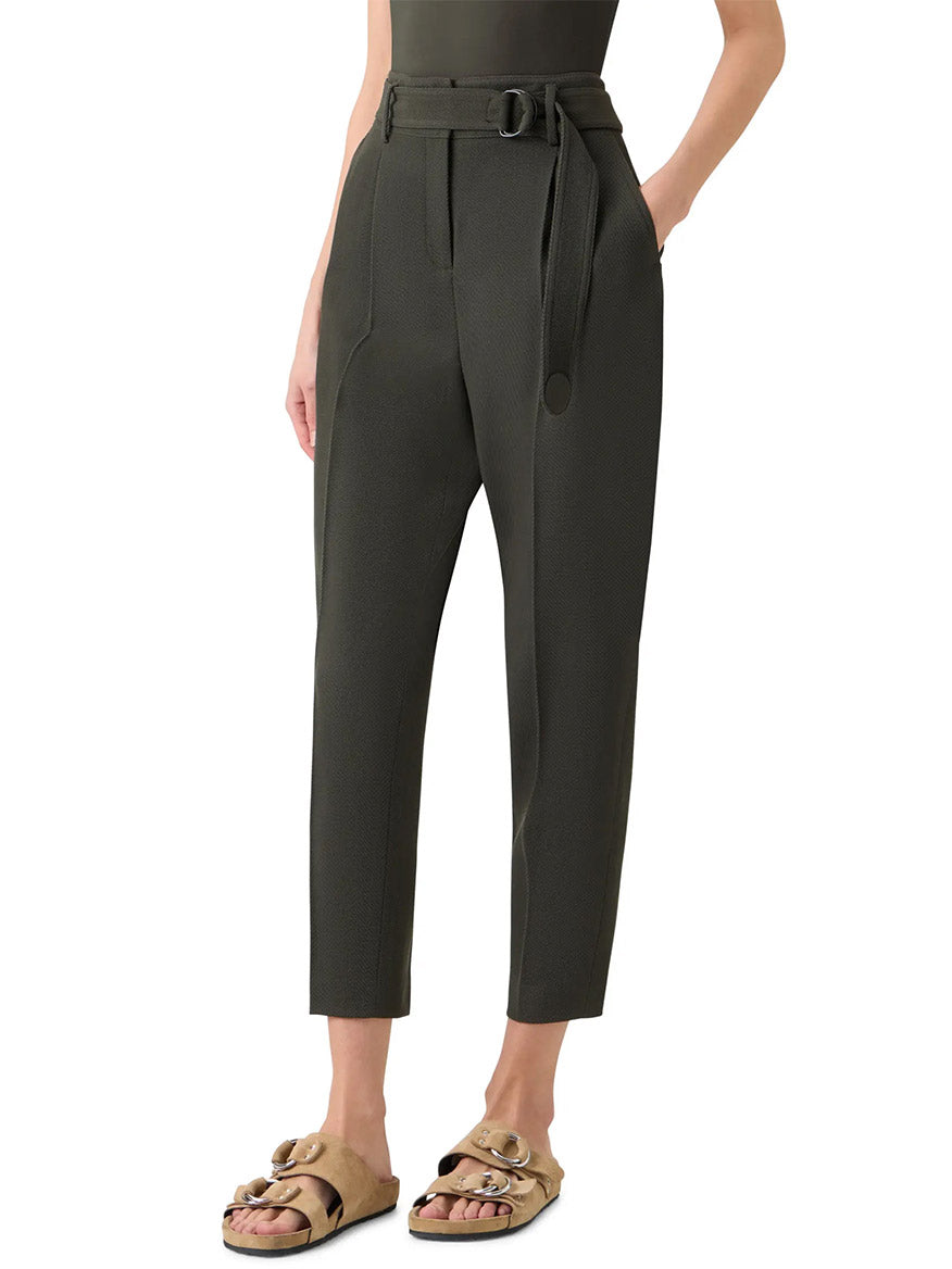 Wearing Akris Punto Fred Belted High Rise Ankle Pants in olive and tan buckle-detail slide sandals, a person stands against a plain background.