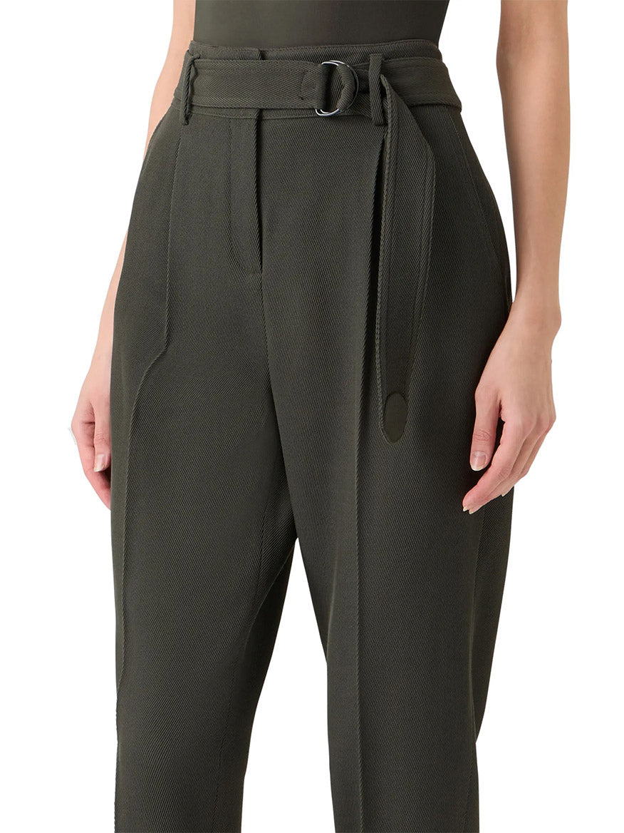A person wearing the Akris Punto Fred Belted High Rise Ankle Pants in Olive, featuring a belted waist, side pockets, and a tapered silhouette from waist to mid-thigh.