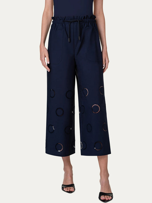 Woman wearing Akris Punto Frey Drawstring Pants with Circle Eyelets in Navy and black sandals standing against a plain background.