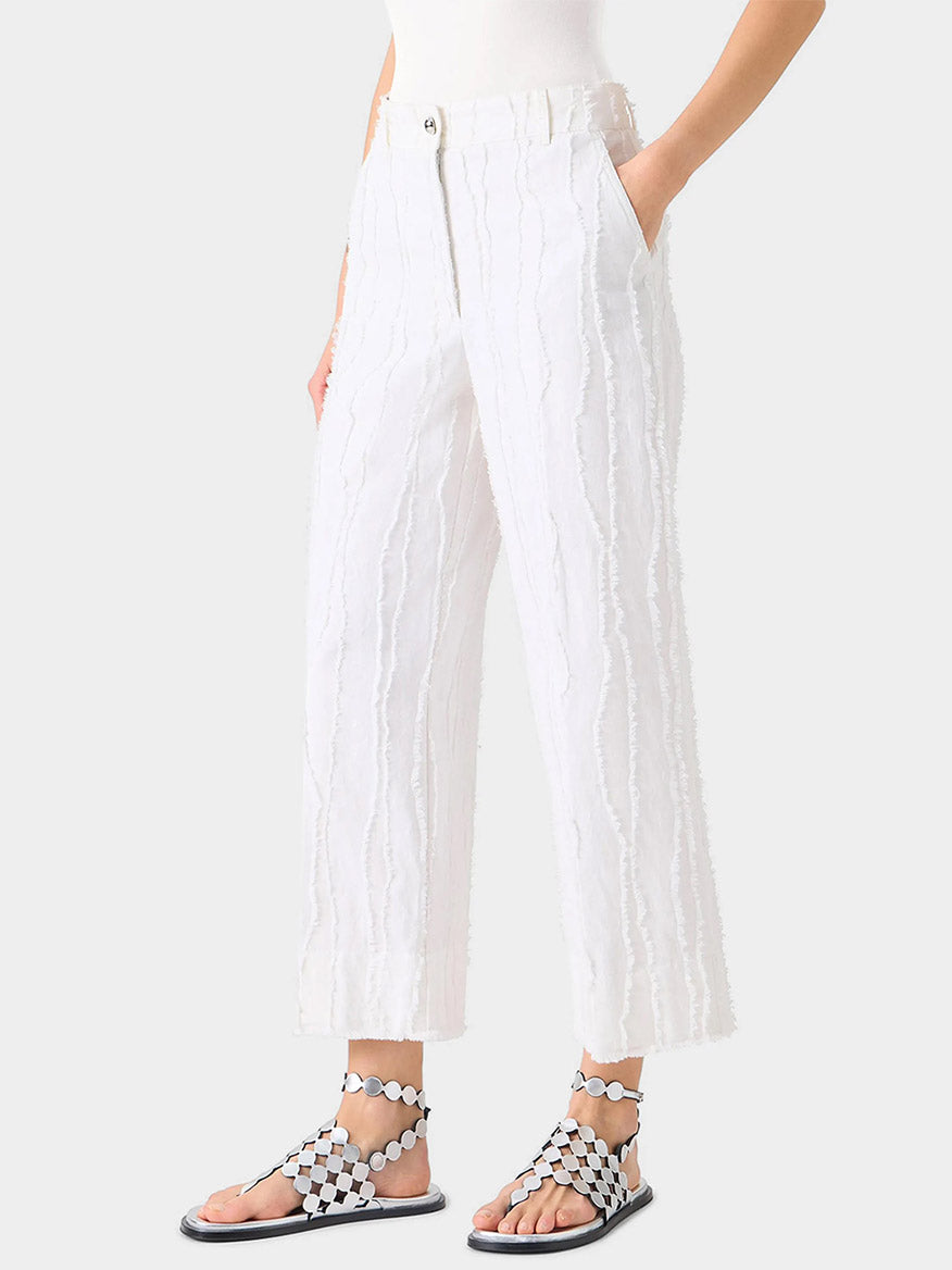 A person wearing Akris Punto Chiara Fringed Wave Jacquard Wide Leg Pants in Cream, a white top, and black-and-white geometric flat sandals stands with hands in pockets.
