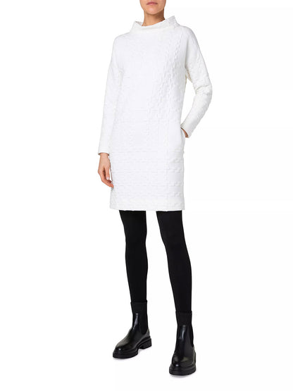 Person wearing an Akris Punto Glencheck 3D Jersey Oversize Dress in Cream, black leggings, and black ankle boots, standing against a white background.