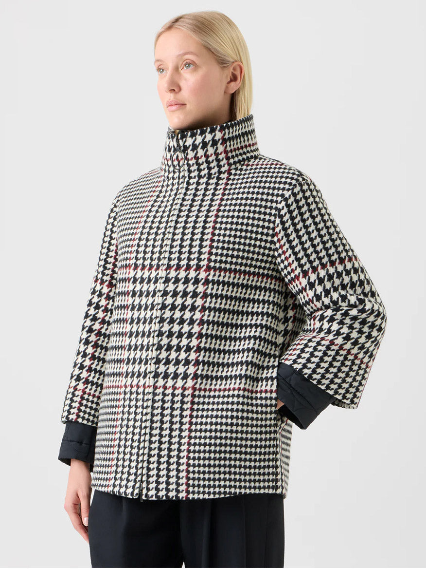 A person with straight blonde hair wears the Akris Punto Glencheck 2-in-1 Car Coat in Black/Cream/Vermillion and black pants, standing against a plain light background.