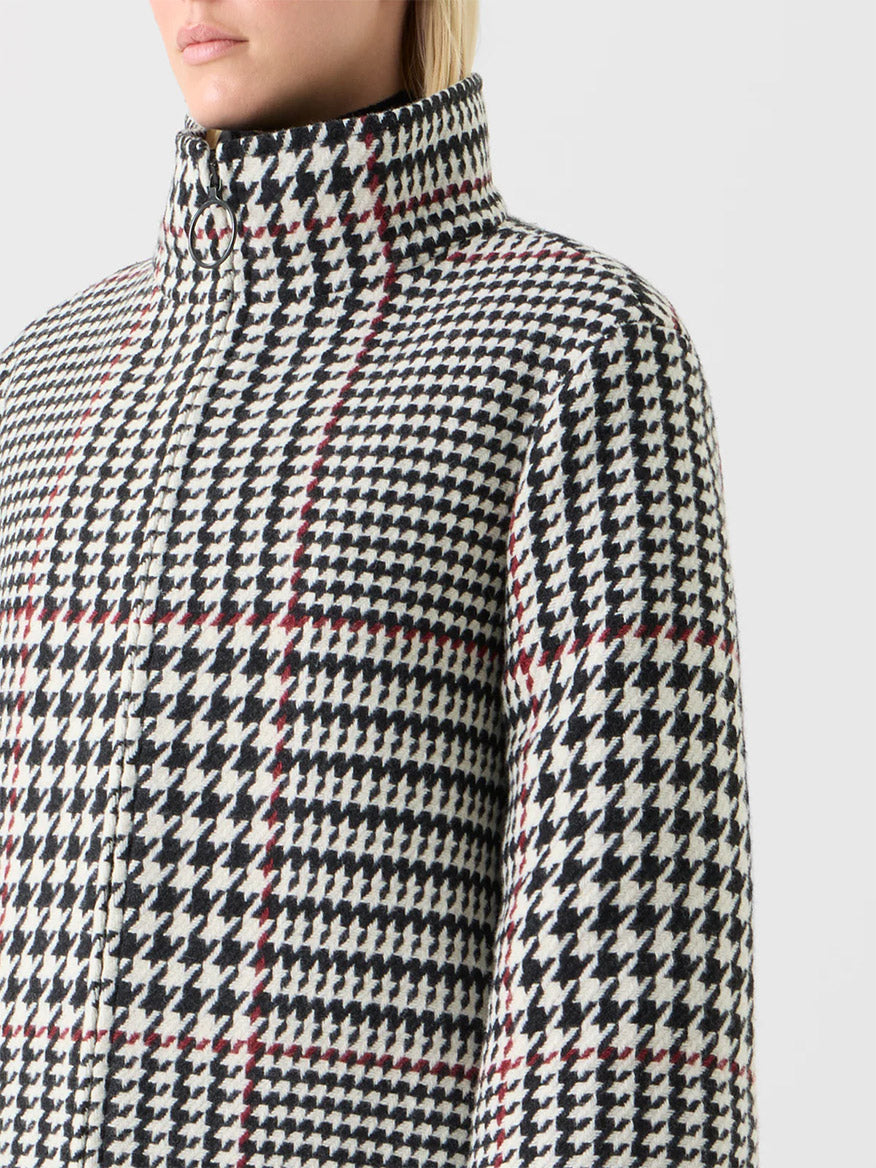 Close-up of a person wearing the Akris Punto Glencheck 2-in-1 Car Coat in Black/Cream/Vermillion, featuring a high collar, black-and-white houndstooth glen plaid with vermillion lines, and a boxy silhouette, against a plain background.