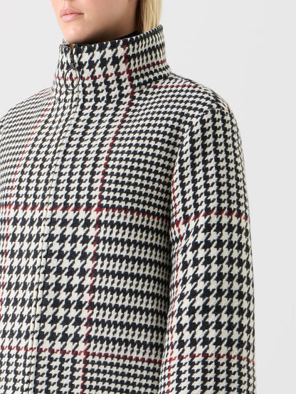Close-up of a person wearing the Akris Punto Glencheck 2-in-1 Car Coat in Black/Cream/Vermillion, featuring a high collar, black-and-white houndstooth glen plaid with vermillion lines, and a boxy silhouette, against a plain background.