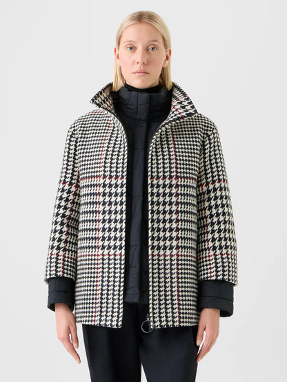 A person with straight blond hair and a neutral expression wears the Akris Punto Glencheck 2-in-1 Car Coat in Black/Cream/Vermillion over a black quilted jacket, standing forward.