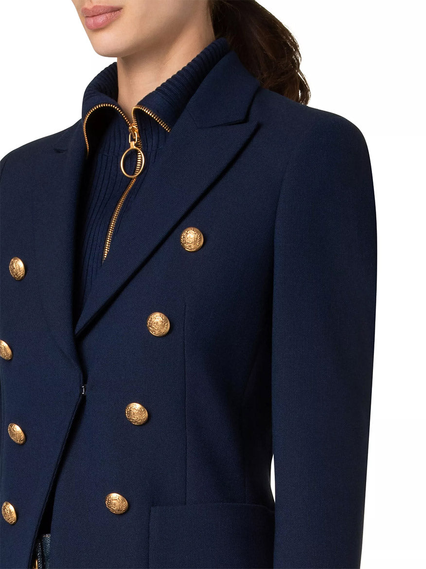 An individual wearing an Akris Punto Illusion Peak Lapel Blazer with gold buttons in navy, paired with a zippered sweater.