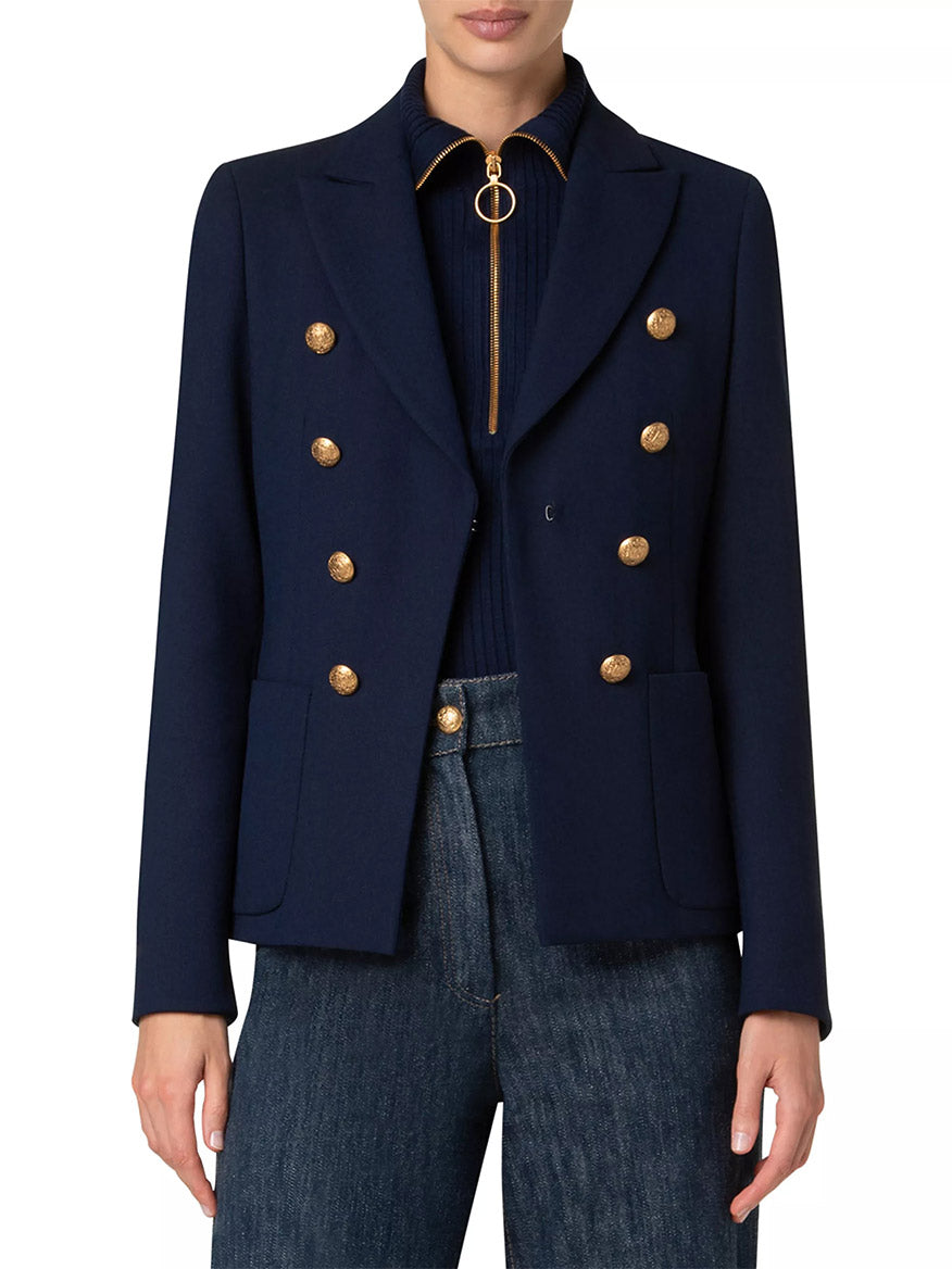 A person wearing an Akris Punto Illusion Peak Lapel Blazer with gold buttons in navy over a dark top, paired with blue jeans.