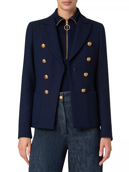 A person wearing an Akris Punto Illusion Peak Lapel Blazer with gold buttons in navy over a dark top, paired with blue jeans.