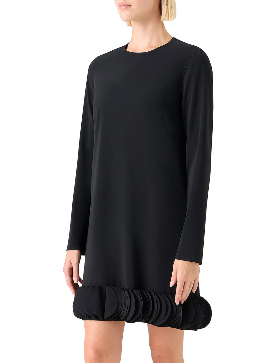 A woman wears the Akris Punto Lasercut 3D Dot Crepe Minidress in black, featuring long sleeves, a round neckline, and layered circular 3D dot trim along the hem.
