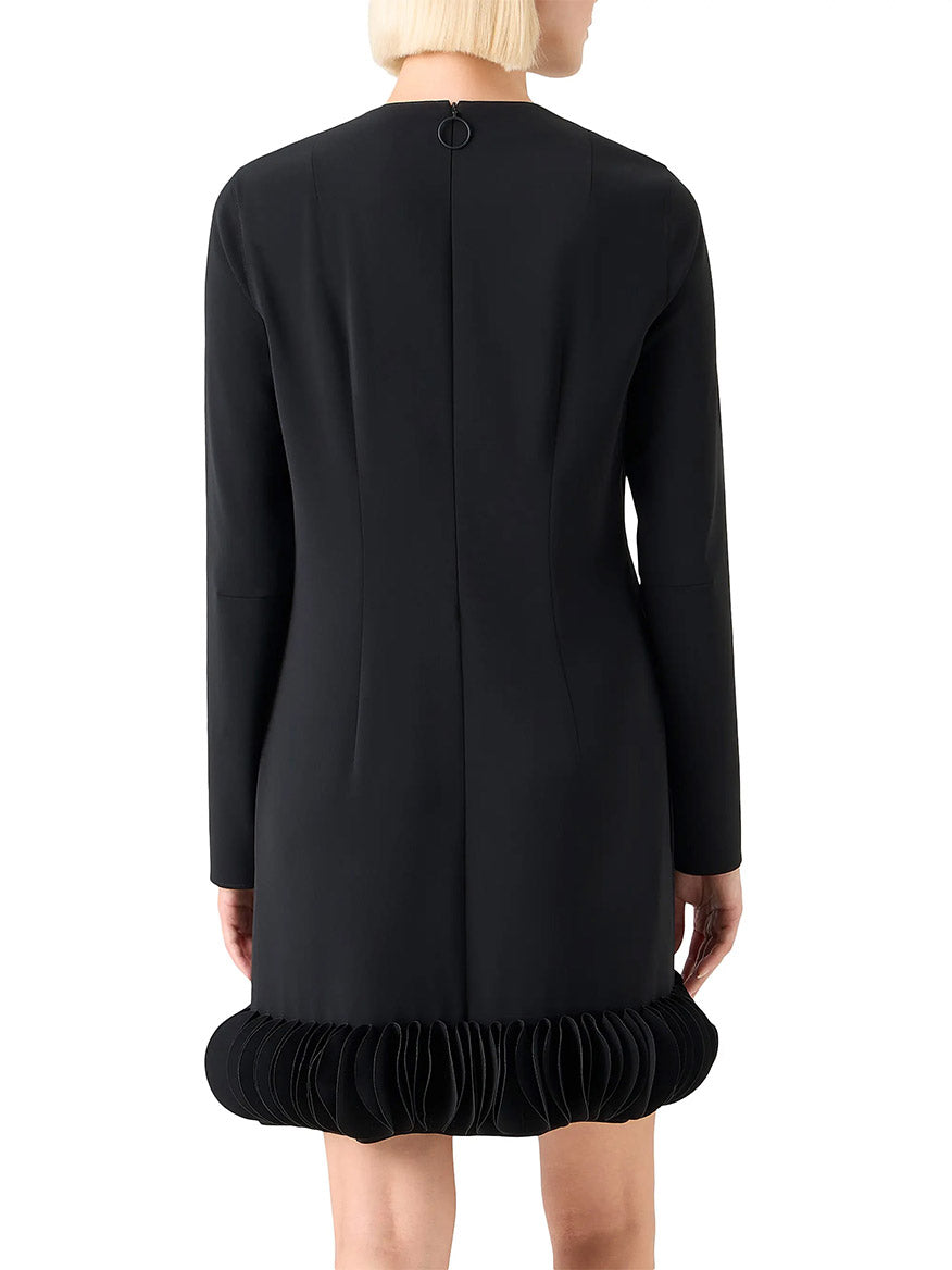 Someone wearing the Akris Punto Lasercut 3D Dot Crepe Minidress in black, a long-sleeve style with a pleated hem, shown from the back.