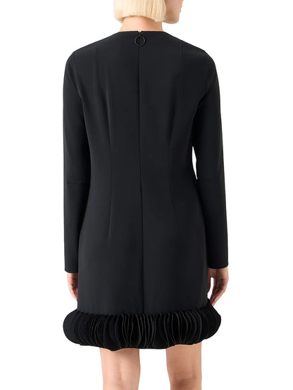 Someone wearing the Akris Punto Lasercut 3D Dot Crepe Minidress in black, a long-sleeve style with a pleated hem, shown from the back.