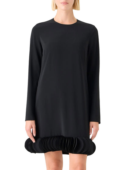 A woman models the Akris Punto Lasercut 3D Dot Crepe Minidress in black, featuring long sleeves, a round neckline, and unique pleated 3D dot trim on its layered circular hem, set against a plain background.