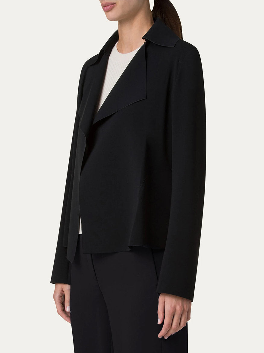 A person stands against a plain background, wearing the Akris Punto Signature Lasercut Biker Jacket in black over a white top and paired with black pants.