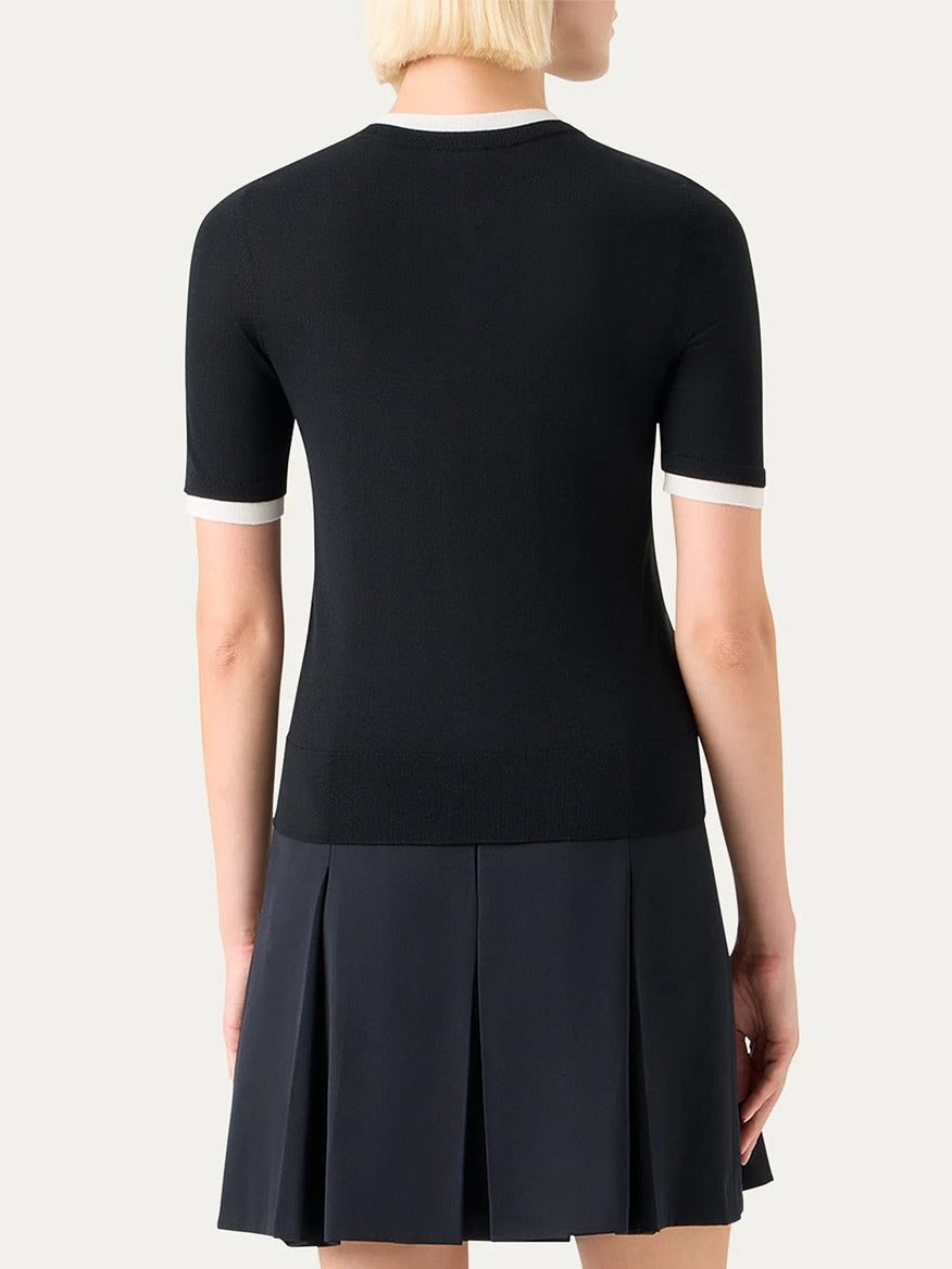 A person with short blonde hair is shown from the back, wearing an Akris Punto Layered Short-Sleeve Knit Sweater in Black/Cream and a dark pleated skirt.