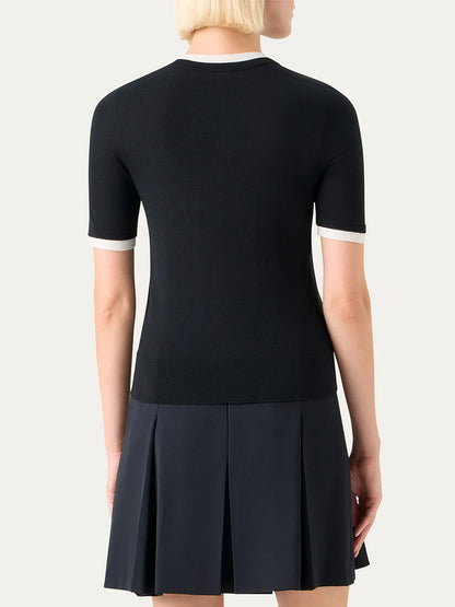 A person with short blonde hair is shown from the back, wearing an Akris Punto Layered Short-Sleeve Knit Sweater in Black/Cream and a dark pleated skirt.