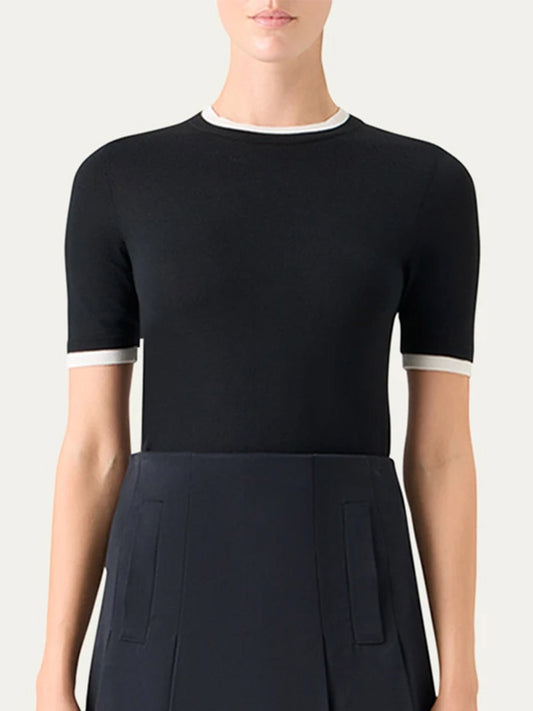 A person wearing the Akris Punto Layered Short-Sleeve Knit Sweater in Black/Cream, featuring a fitted design with white trim, paired with a dark skirt.