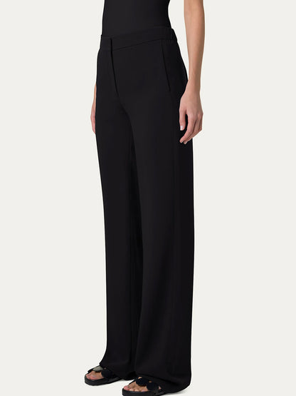 Wearing Akris Punto Marla Wide Straight Lasercut Trousers in black with an elastic waistline and a matching top, a person poses against a light gray background.