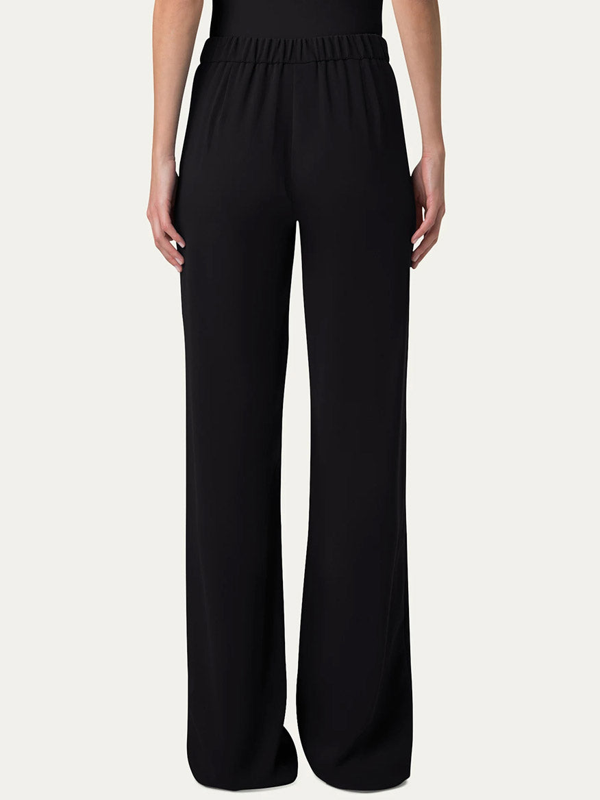 A person stands against a plain white background wearing Akris Punto Marla Wide Straight Lasercut Trousers in black with an elastic waistline, paired with a matching black top.