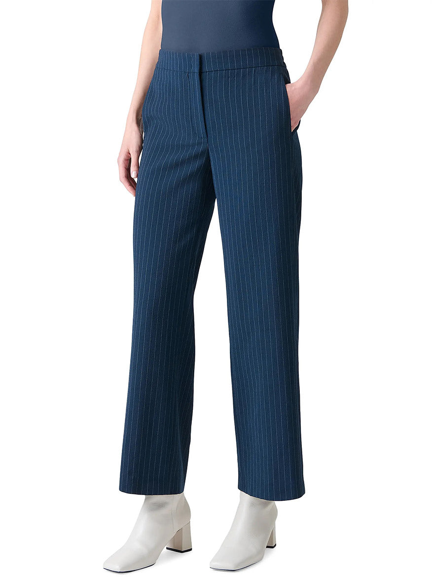 A person wearing Akris Punto Marlon Pinstripe Wide Leg Pant in Navy/Cream, a dark top, and white ankle boots stands with hands in pockets against a plain background.