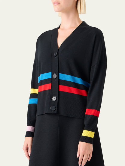 A woman wears the Akris Punto Striped Merino Knit Cardigan in Black Multi, a black V-neck cardigan with colorful blue, red, yellow, and pink horizontal stripes across the body and sleeves.
