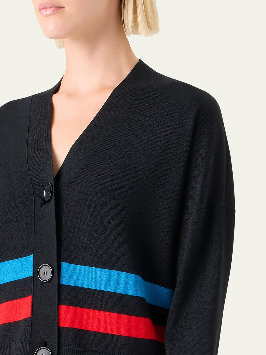 A person wears the Akris Punto Striped Merino Knit Cardigan in Black Multi, featuring blue and red colorblock stripes, large black buttons, and a V-neck. The image shows their upper body and part of their face.
