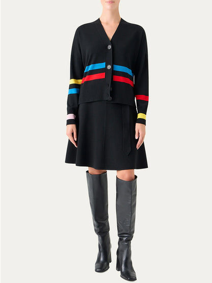 Someone stands against a plain background wearing the Akris Punto Striped Merino Knit Cardigan in Black Multi, paired with a black skirt and black knee-high boots.