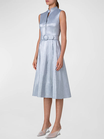 A woman wearing an Akris Punto Metallic Cotton Belted Midi Dress in Silver Blue with a mid-length pleated skirt and white pointed-toe heels.