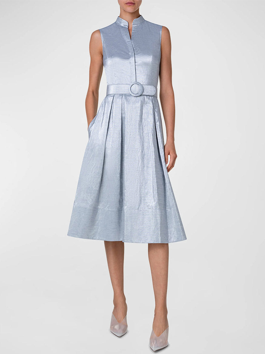 A model wearing an Akris Punto Metallic Cotton Belted Midi Dress in Silver Blue with a mandarin collar and a cinched waist, paired with matching pointed-toe heels. The dress boasts a metallic sheen.