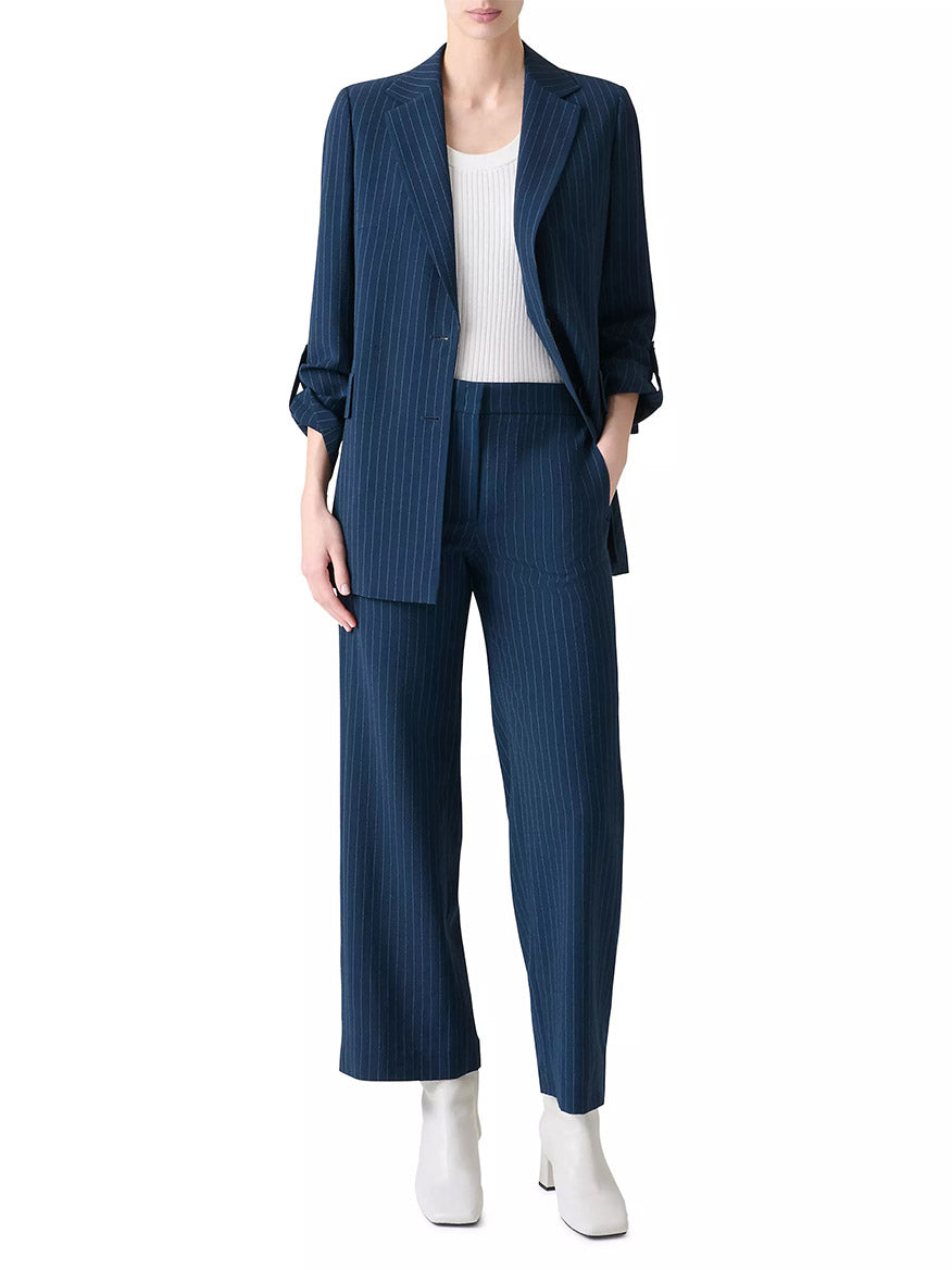 A person wears the Akris Punto Pinstripe Virgin Wool Jacket in Navy/Cream over a white ribbed top with white ankle boots, standing against a plain background.