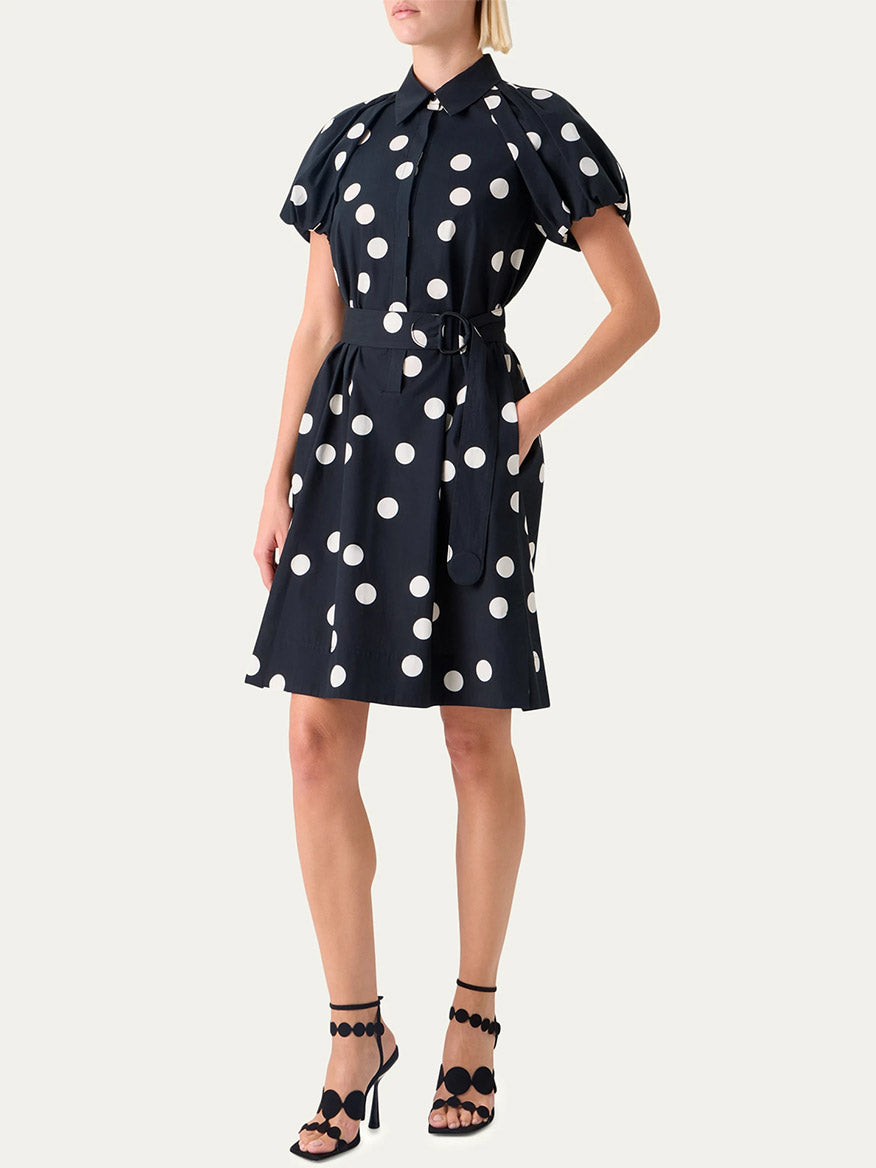 A woman wears the Akris Punto Polka Dot Balloon Sleeve Shirtdress in Black/Cream, styled with black open-toe heels featuring circular ankle straps.