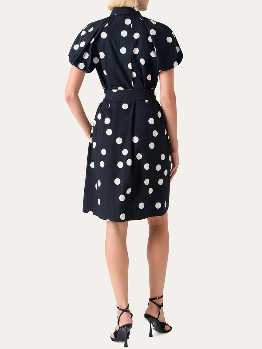 A woman stands with her back to the camera, wearing the Akris Punto Polka Dot Balloon Sleeve Shirtdress in Black/Cream and black high-heeled sandals for an elegant look.