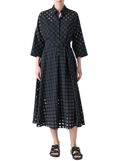 A person wearing the Akris Punto Midi Polka Dot Organzino Belted Dress in Black/Cream with black sandals stands against a white background.