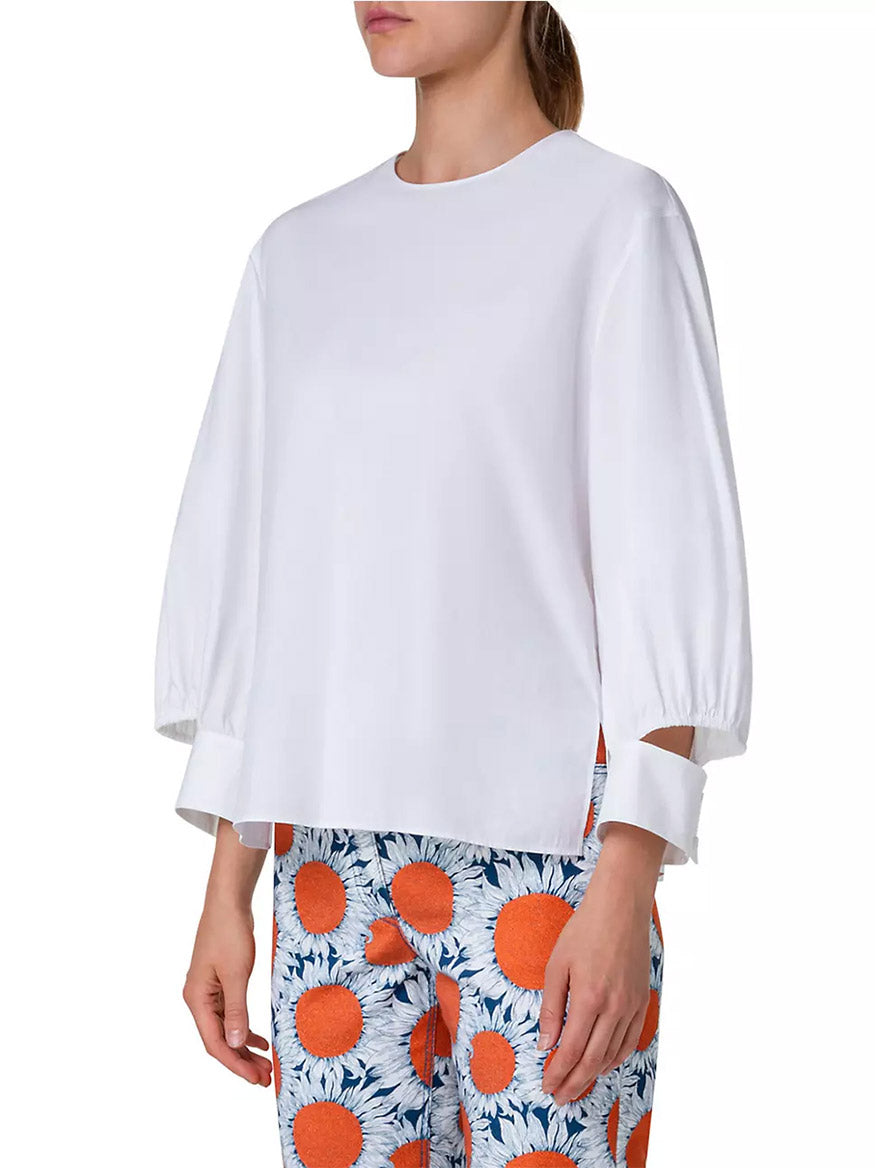A woman is wearing an Akris Punto Puff Sleeve Cotton Poplin Blouse in Cream with floral pants.