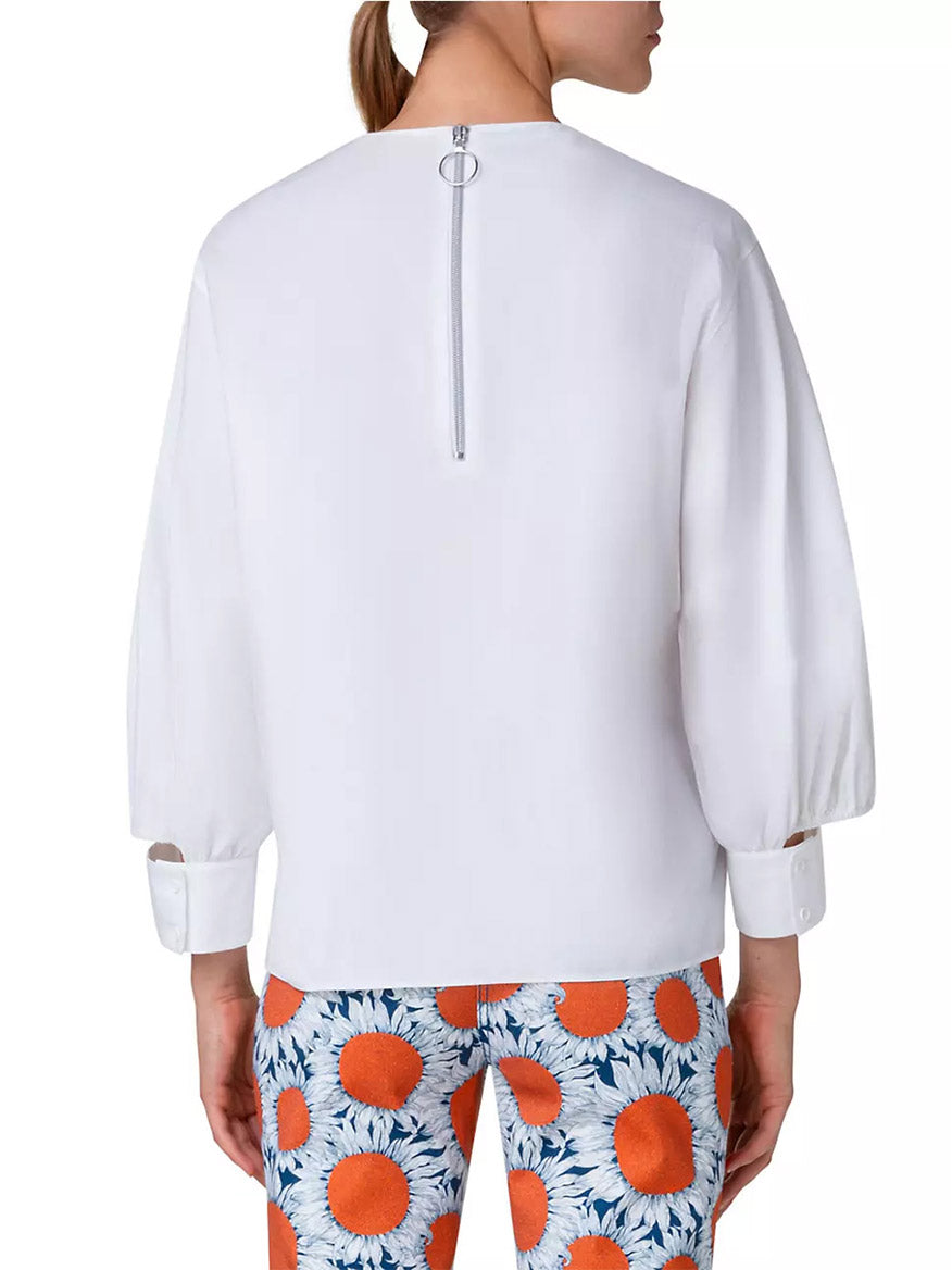 The back of a woman wearing an Akris Punto Puff Sleeve Cotton Poplin Blouse in Cream with long puff sleeves and orange floral pants.