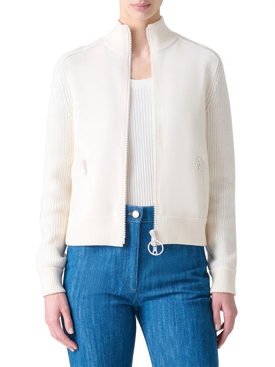A person wearing the Akris Punto Rib-Knit Wool Zip Cardigan in cream over a matching ribbed top and blue jeans, standing against a white background.