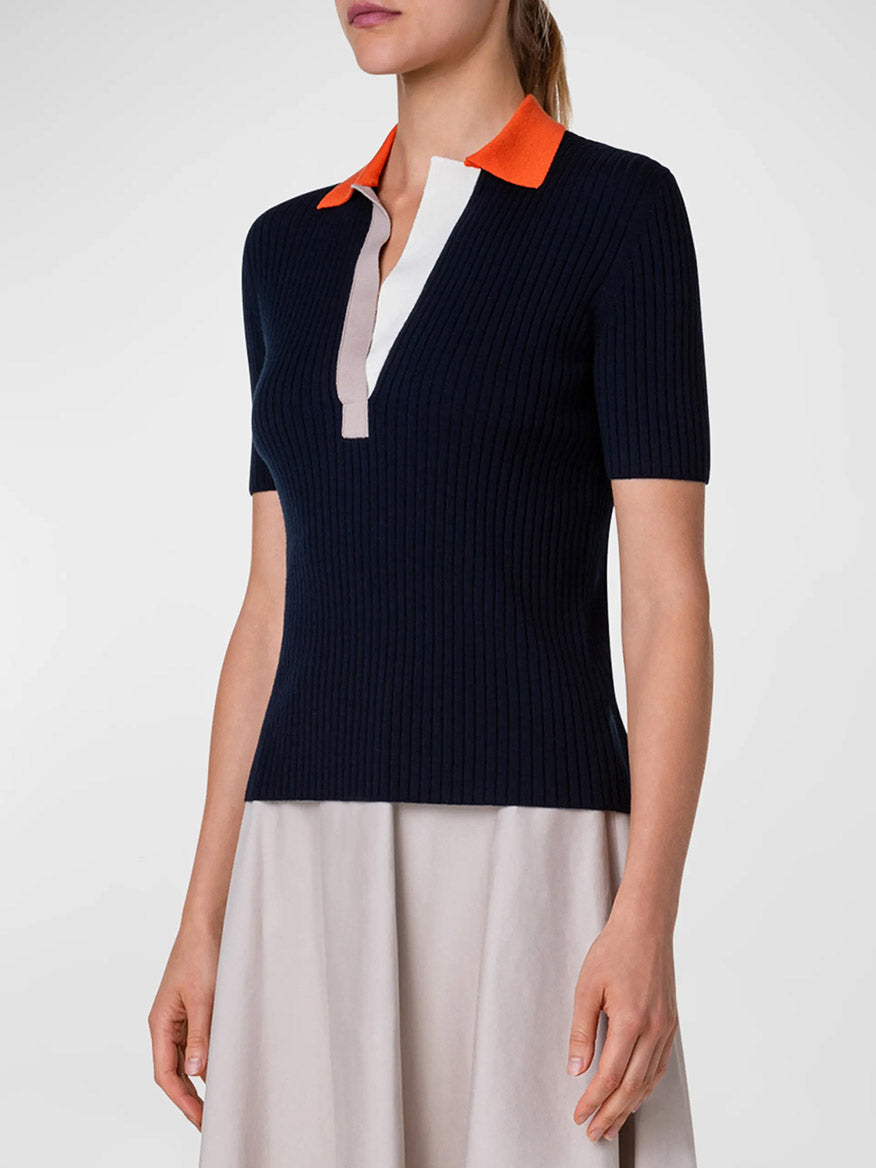 A woman wearing an Akris Punto Ribbed Wool Polo Top in Navy Multi and orange skirt with contrast detailing.