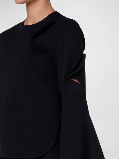 The woman is wearing a black Akris Punto Cutout Blouse with Bird Applique in Black with bell sleeves.