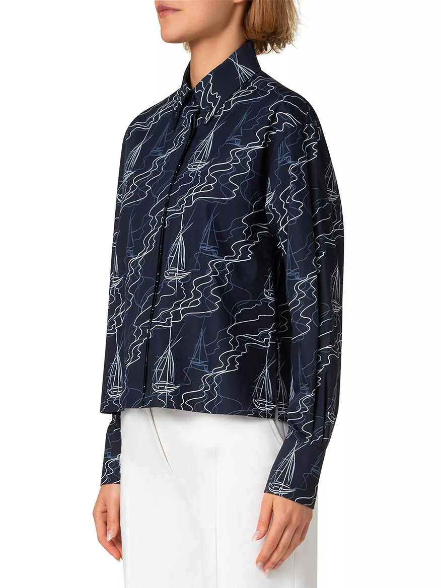 Someone in an Akris Punto Sailboat Print Poplin Top in Navy/Cream, featuring a stylish johnny collar and sailboat pattern, paired with white pants, stands against a plain background.