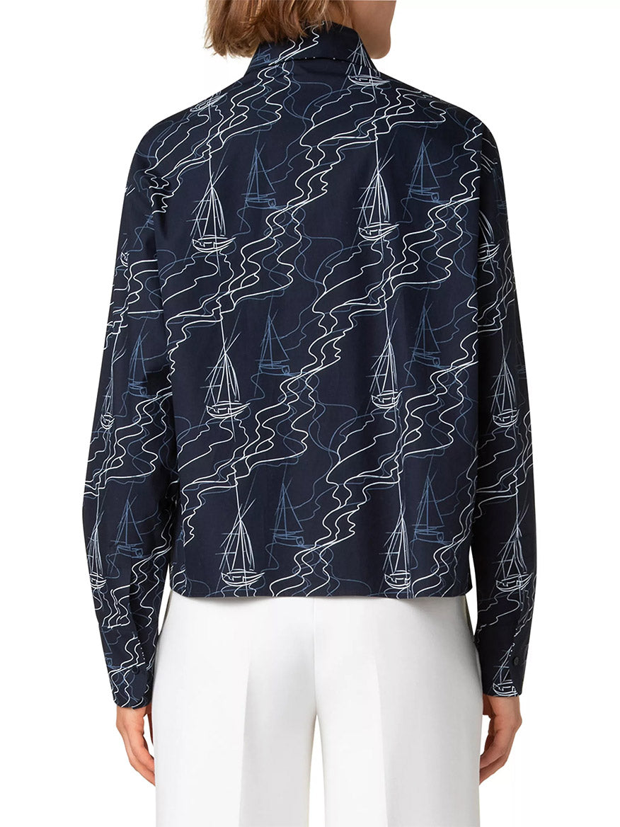 The Akris Punto Sailboat Print Poplin Top in Navy/Cream, featuring a sailboat pattern and a relaxed drop-shoulder silhouette, is paired with white pants from a back view. This dark blue cotton poplin tunic combines style and comfort effortlessly.