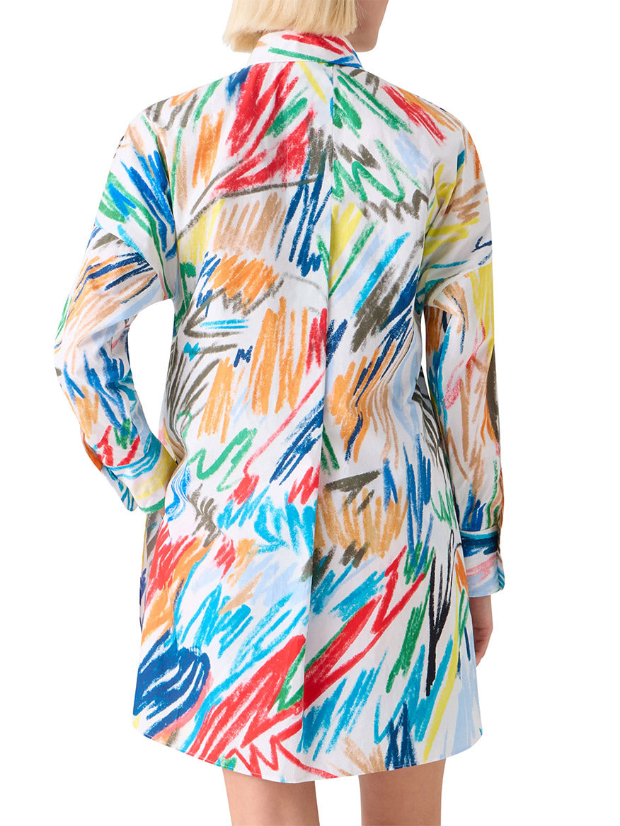 A person wearing the Akris Punto Scribble Print Tunic Blouse in Cream Multi, featuring a long-sleeve design and colorful abstract pattern, stands facing away from the camera.