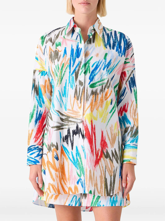 A person wearing the Akris Punto Scribble Print Tunic Blouse in Cream Multi, featuring long sleeves, button-up style, and a colorful scribble pattern in blue, orange, yellow, pink, and green on a white background.