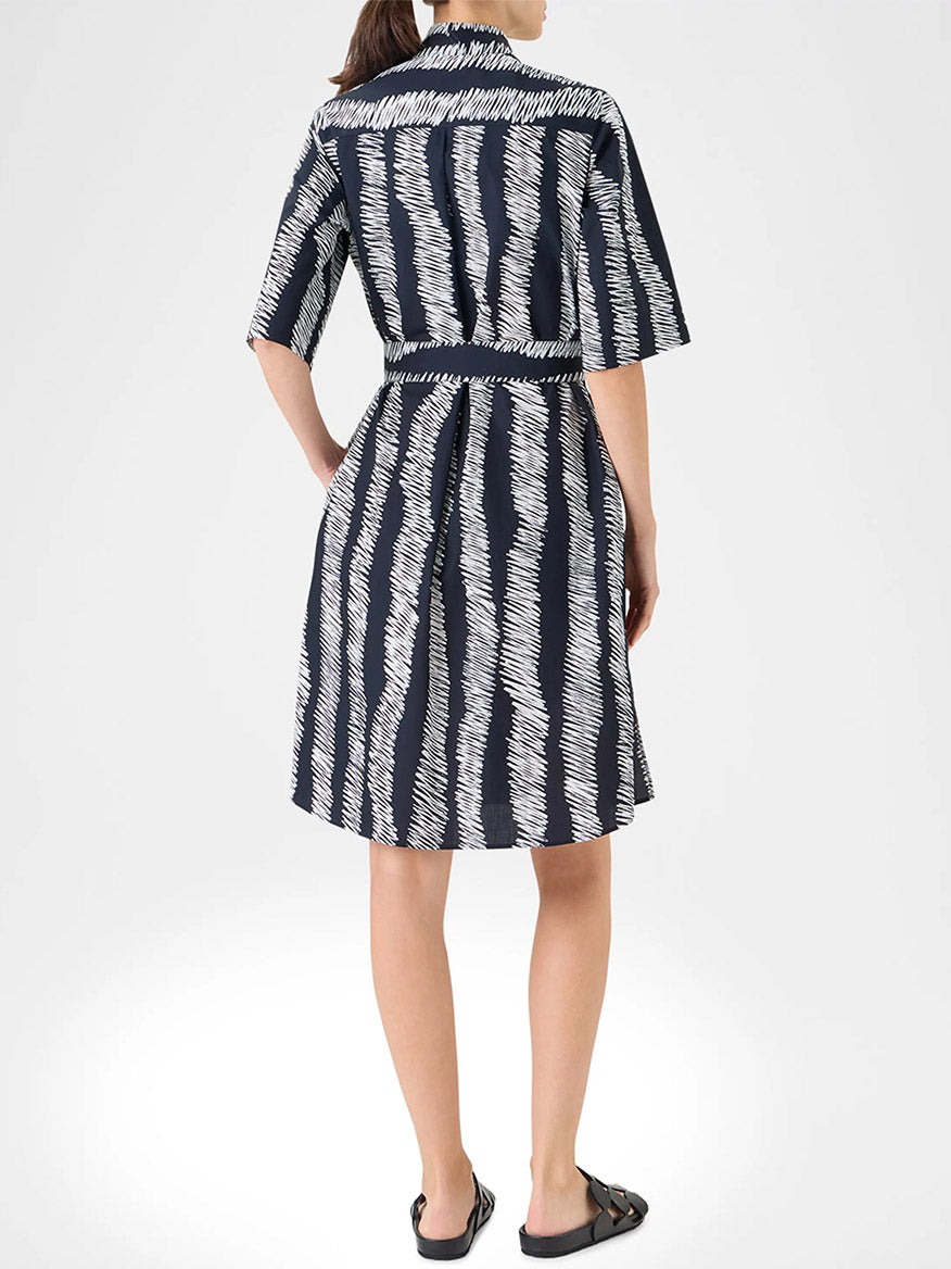 A person stands facing away, wearing the Akris Punto Scribble Wave Shirt Dress in Black/Cream with a belt and black sandals.