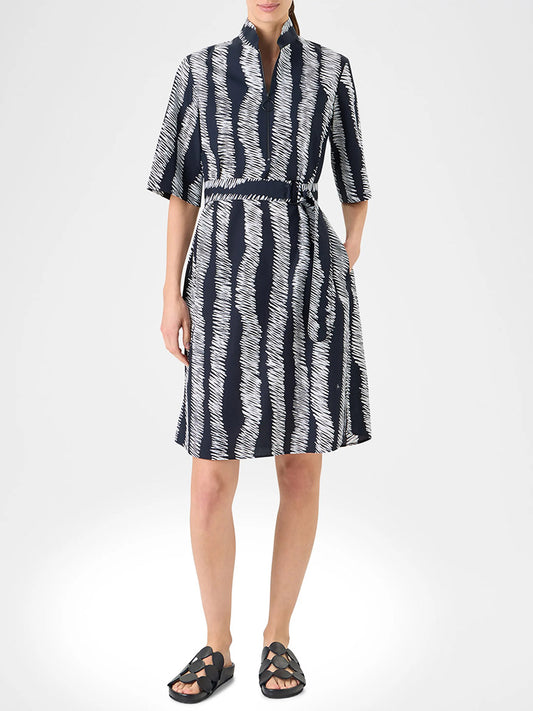 A person wears the Akris Punto Scribble Wave Shirt Dress in Black/Cream, a knee-length, short-sleeve shirtdress with a scribble striped print, paired with black sandals.