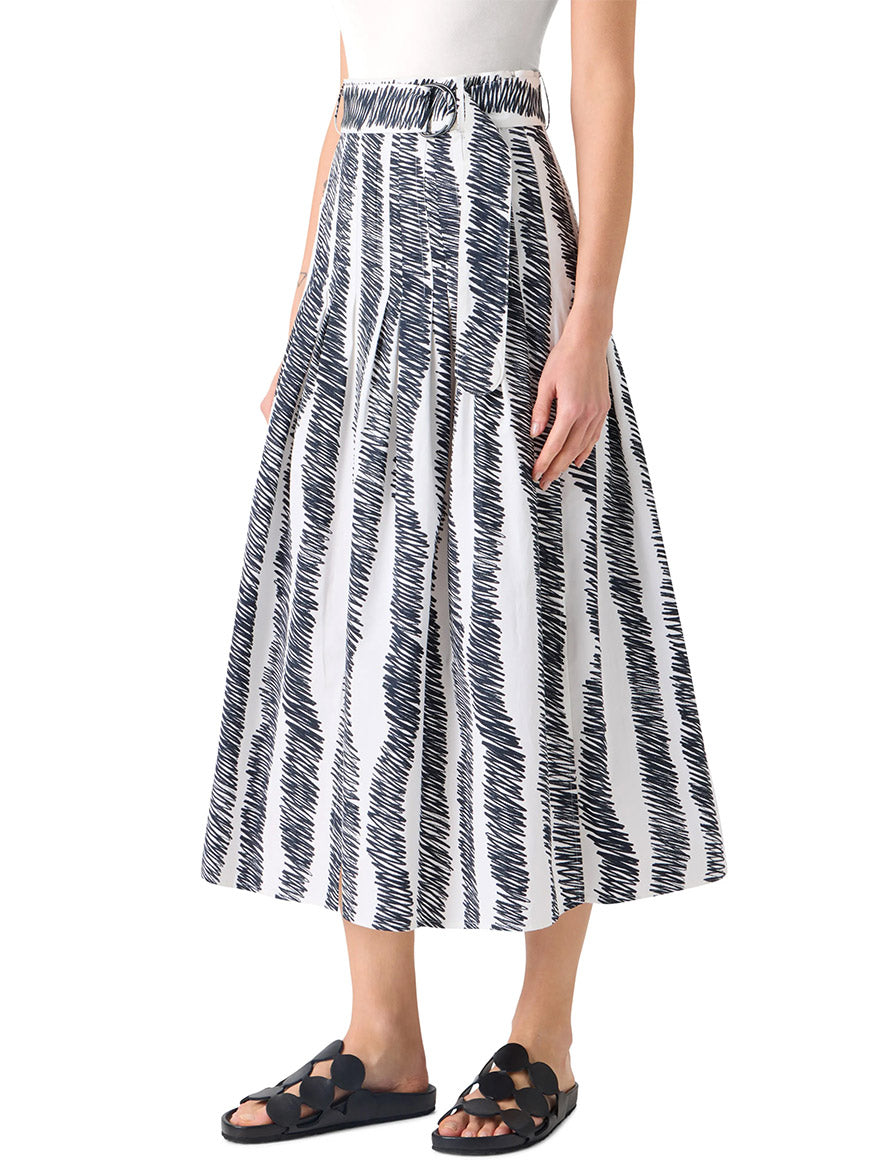 A person wears a white sleeveless top and the Akris Punto Scribble Wave Print Midi Skirt in Cream/Black, paired with black sandals.