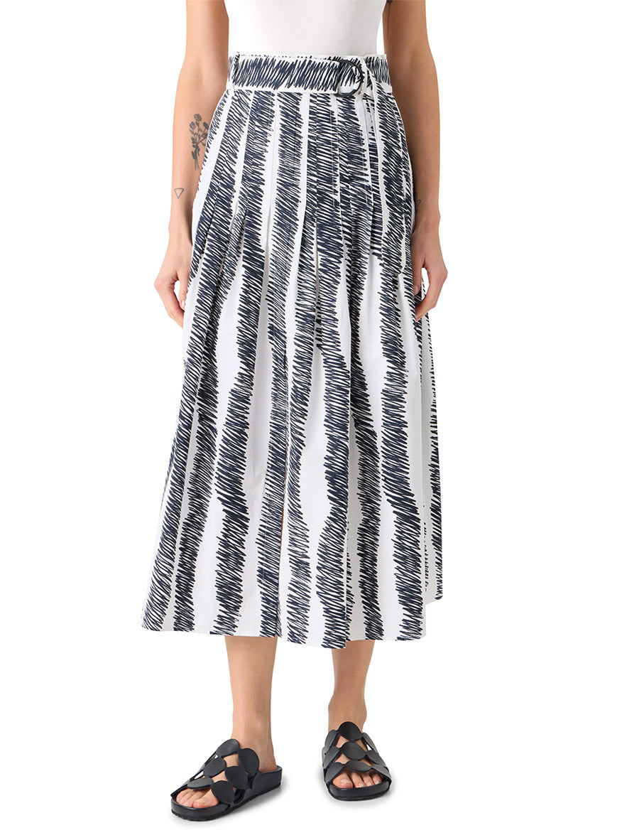 A person wears a white sleeveless top, the Akris Punto Scribble Wave Print Midi Skirt in Cream/Black, and black sandals.