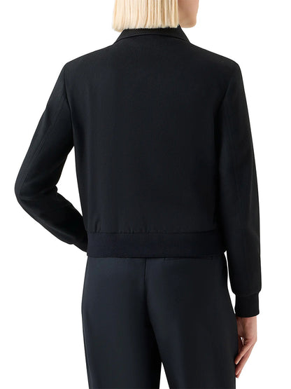 A person with short blonde hair is seen from the back wearing the Akris Punto Wool/Cashmere Short Bomber Jacket in Black and black pants, featuring rib-knit trim.